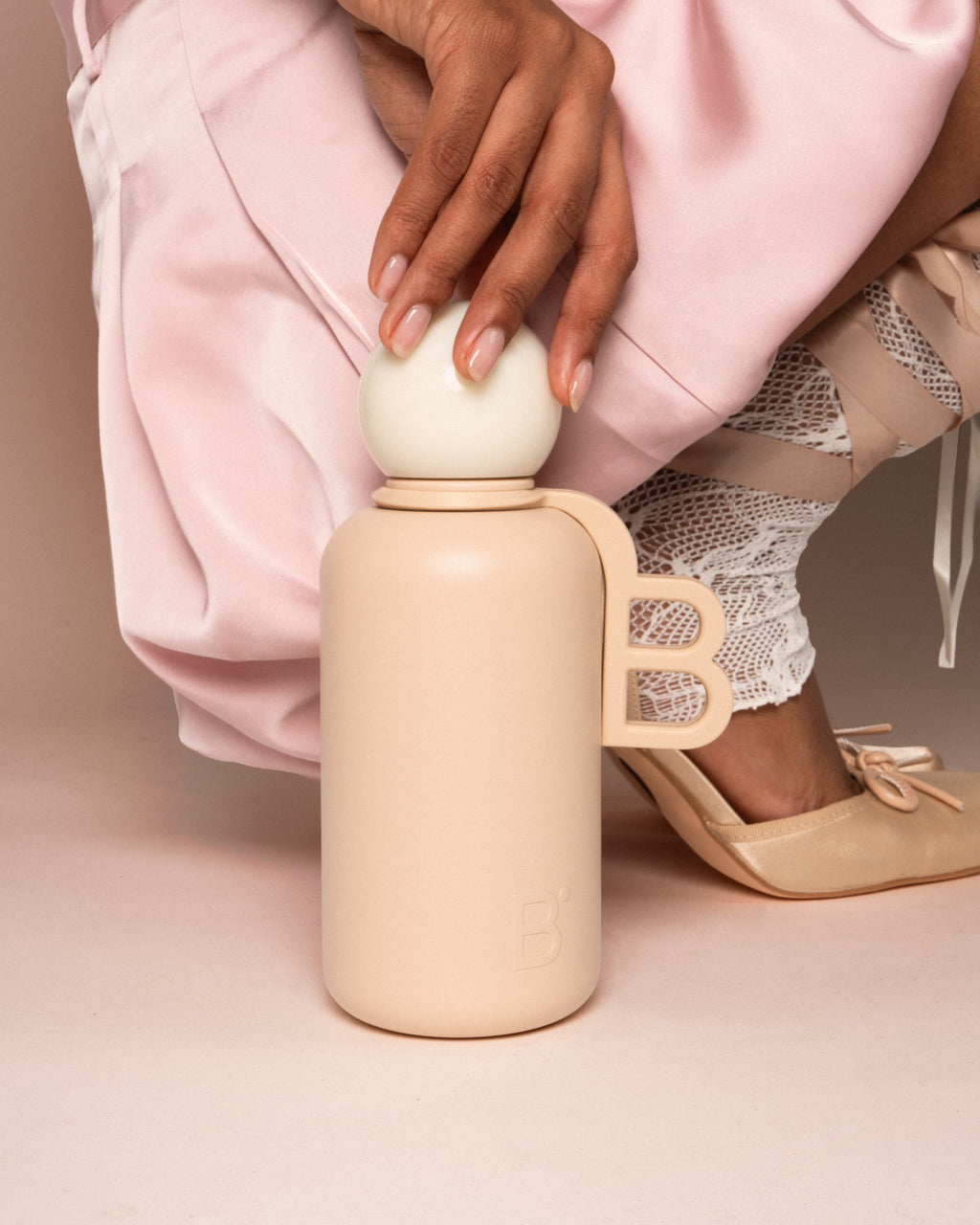 Celine luxury water bottle held in hand, beige stainless steel with rounded cap